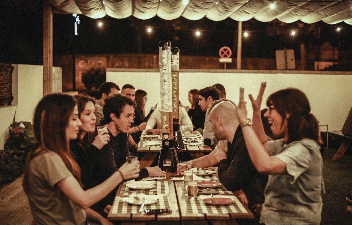 Mesa de amigos a rir no jardim, com torres de cerveja